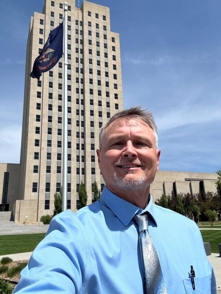 Paul takes a selfie in front of the Capitol Building in Bismarck. The ND state flag waves behind him as well.